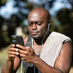 A man using a smartphone with earphones, enjoying music outdoors. The scene captures a moment of technology and relaxation.