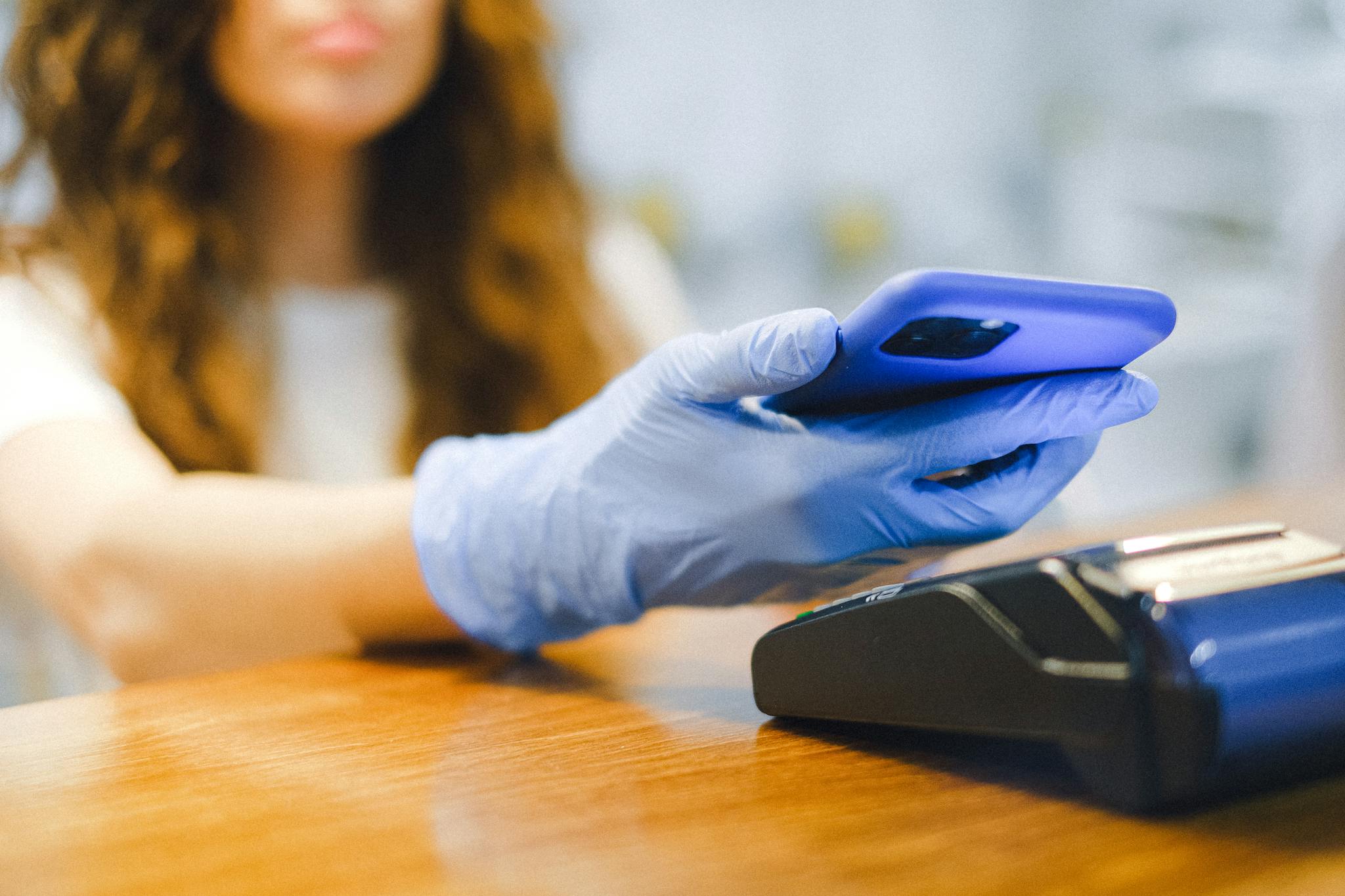 Woman using a smartphone for contactless payment in a store while wearing protective gloves.